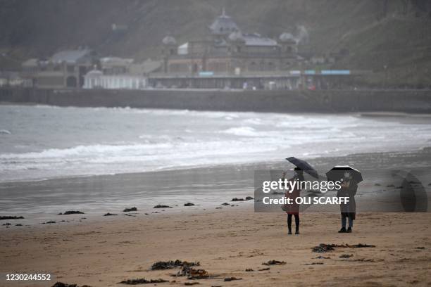 People wearing a face mask or covering due to the COVID-19 pandemic, shelter from the rain as they walk on the beach in in Scarborough, north east...