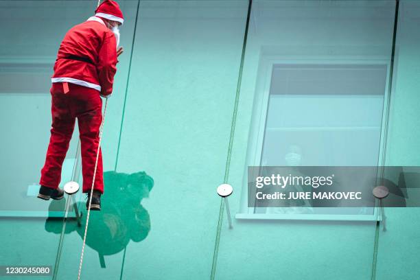 Man dressed as a Santa Claus waves to a child as he descends from the roof of the paediatric clinic in Ljubljana, Slovenia on December 21, 2020.