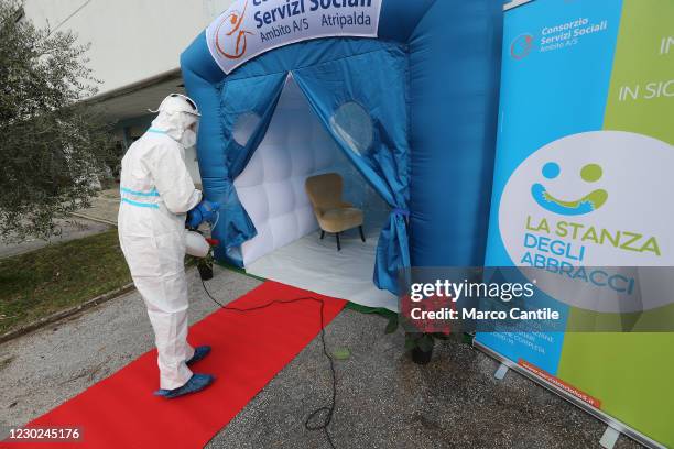 Man in a protective suit sanitizes the Room of Hugs, a structure to allow relatives of a retirement home for the elderly, to meet their loved ones...