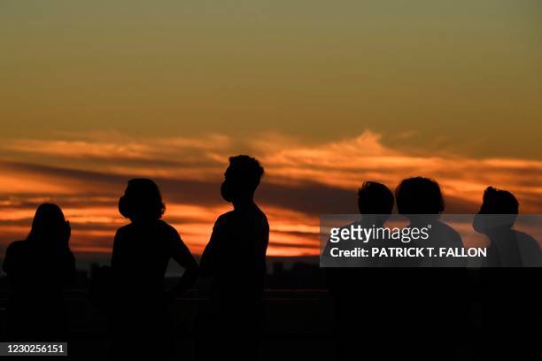 People wearing face masks watch the sunset as they wait to see the planets Jupiter and Saturn during the great conjunction at the Griffith...