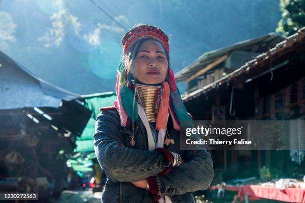 Long neck woman stands inn an alley with souvenir shops in the Huay Sua Tao village in northern Thailand. These women belong to the Padaung tribe ,...