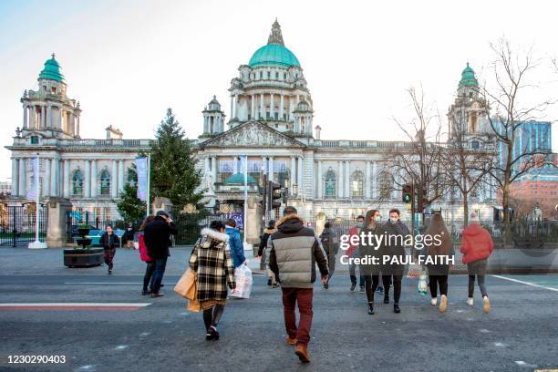 Pedestrians and shoppers cross a road beside Belfast City Hall in Belfast city centre on Christmas Eve, December 24, 2020 as the Province prepares to...