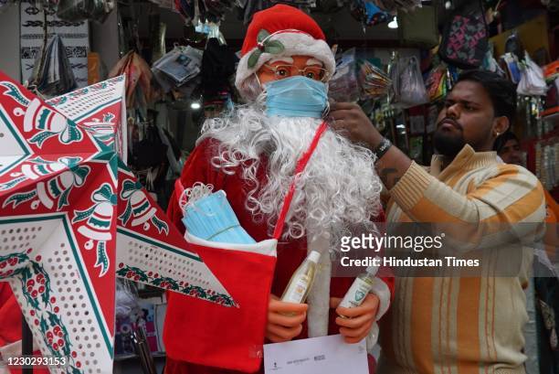 Man put a face mask on a santa claus for sale ahead of Christmas amid coronavirus outbreak, at Chhota Mall, Sigra road on December 24, 2020 in...