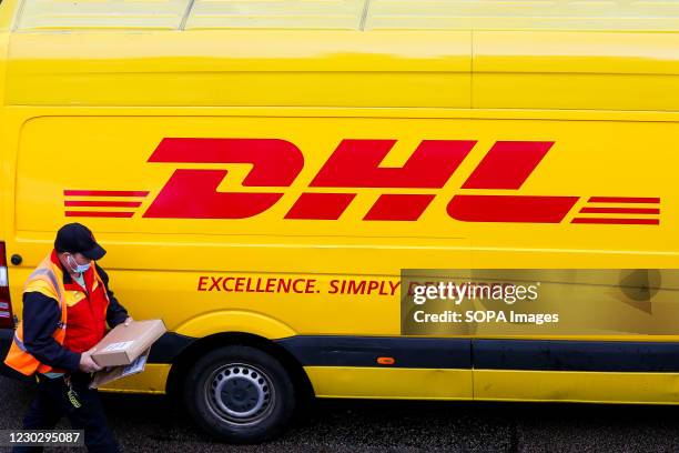 Delivery driver with a parcel in his hand stands next to the DHL van in London.