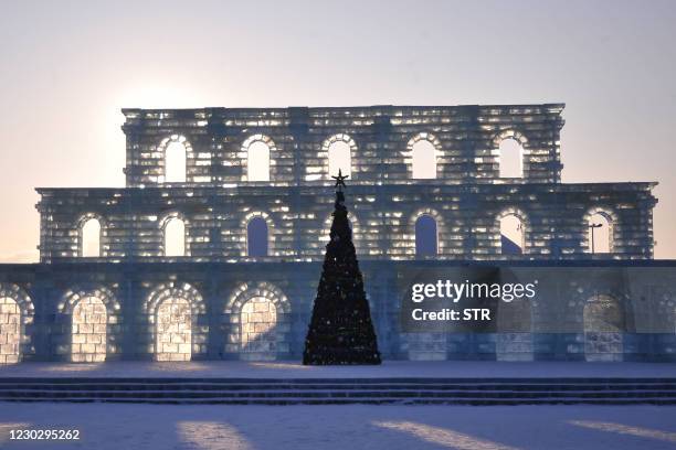 This photo taken on December 24, 2020 shows a Christmas tree in front of ice sculptures ahead of the Harbin International Ice and Snow Festival in...