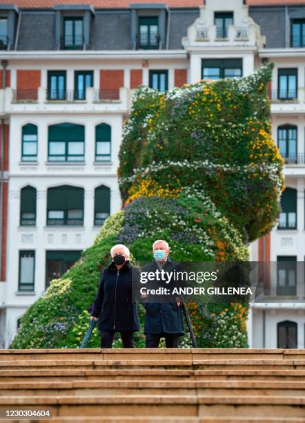 Couple walks past US artist Jeff Koons' "Puppy" which these days sports a flowery face mask, at the Guggenheim Bilbao Museum in the Spanish Basque...