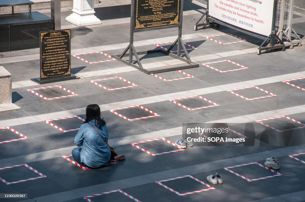 A woman sits on a social distancing square while praying in...