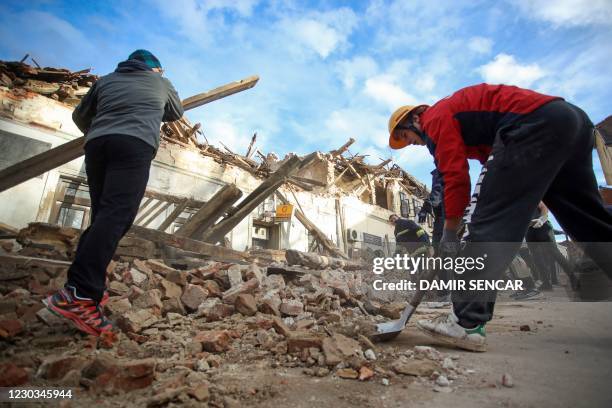 People help cleaning rubble next to damaged buildings in Petrinja, some 50kms from Zagreb, after the town was hit by an earthquake of the magnitude...