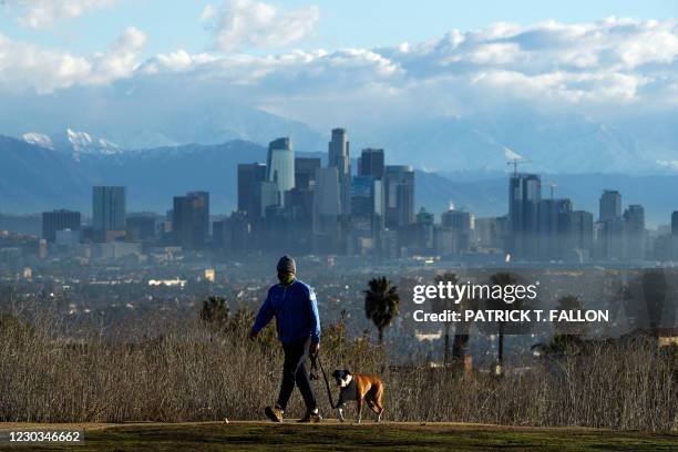 Person walks a dog as snow-topped mountains stand behind the Los Angeles downtown skyline after sunrise following heavy rains as seen from the...