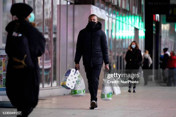 Man with groceries and toilet paper is seen walking past a closed strip mall in Warsaw, Poland on December 29, 2020. On Monday a countrywide...