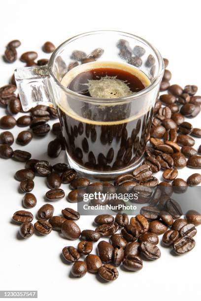 Glass coffee mug with a shot of espresso in the cup next to raw organic Arabica variety coffee beans on white background isolated. Amsterdam, The...