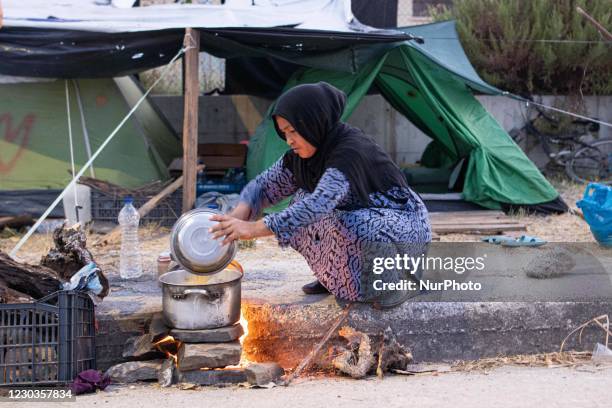 Female refugee is cooking her food over the makeshift fire stove on the road. Refugee and migrants preparing food or tea in makeshift stoves or open...