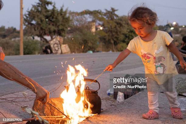 Little girl, a minor asylum seeker from Afghanistan is playing with the fire of heating water for tea and cooking over the fire stove on the road....