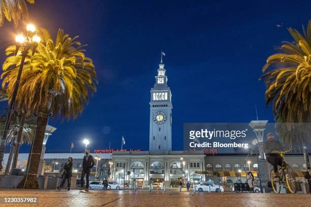 Pedestrians wearing protective masks walk on the Embarcadero in front of the Ferry Building in San Francisco, California, U.S., on Tuesday, Dec. 29,...
