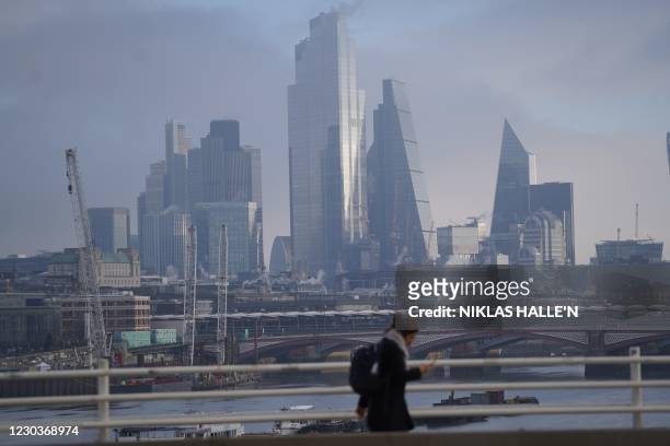 Pedestrians walk along a bridge over the River Thames with skyscrapers and offices of the City of London in the background in London on December 31,...