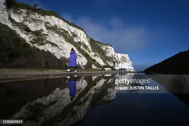 Pedestrians walk at St Margaret's Beach as The White Cliffs are reflected in a puddle in Dover on the south coast of England on December 31, 2020 the...