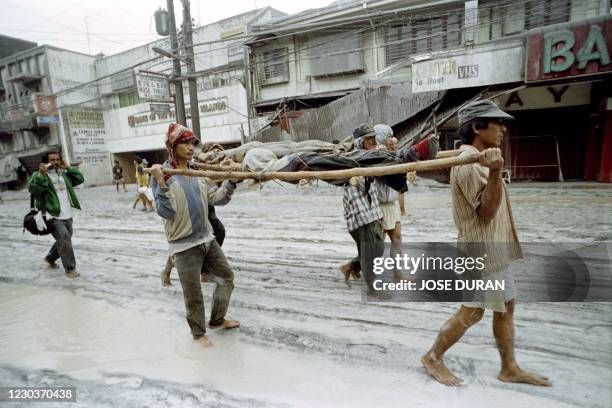 Residents carry the bodies of two victims who were burried in mud and sand, on June 16, 1991 in Olongapo after a major eruption of Mount Pinatubo...