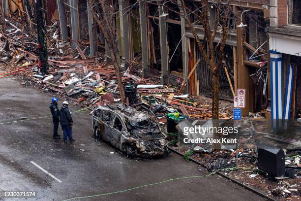 Officers stand next to an invcinerated vehicle and observe damage down to the historic buildings on Second Avenue on Decemeber 31, 2020 in Nashville,...