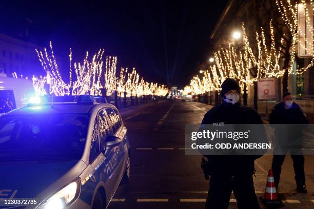 Police block a section of the Unter den Linden boulevard leading to Berlin's landmark Brandenburg Gate, which is illuminated during a concert, on New...