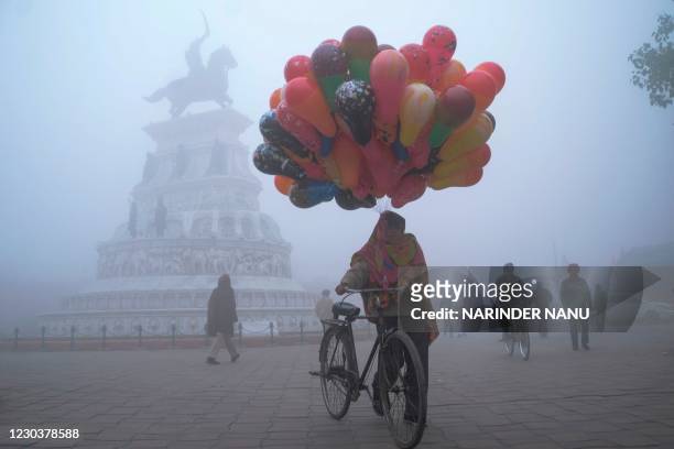 Balloon seller walks along Heritage street amid dense fog on a cold day on New Year's Day, in Amritsar on January 1, 2021.