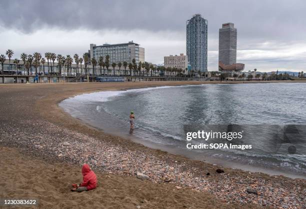 Minor is seen sitting on the sand while his mother prepares for the first swim of the year at Barceloneta Beach As a tradition, some people went to...