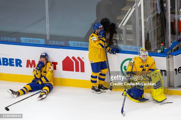 Noel Gunler, Emil Andrae and goaltender Hugo Alnefelt of Sweden react to their loss against Finland during the 2021 IIHF World Junior Championship...