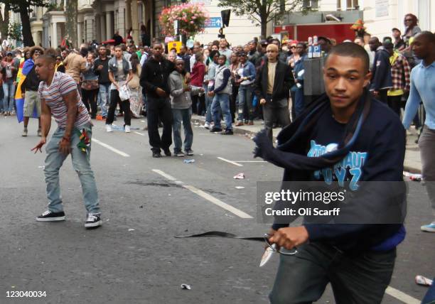 Man carrying a knife avoids being tripped by a member of the public as he runs down the road at the Notting Hill Carnival on August 29, 2011 in...