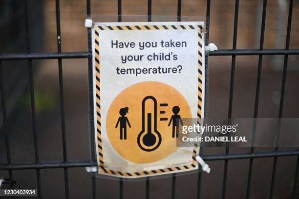 Signage reminding people parents to check their children's temperature because of the coronavirus pandemic is seen on the closed gate of a primary...