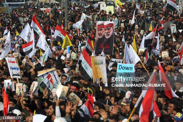 Iraqi demonstrators lift flags and placards as they rally in Tahrir square in the capital Baghdad on January 3 to mark one year after a US drone...