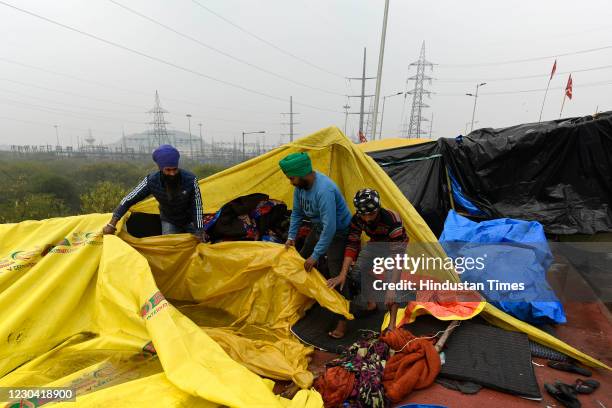 Farmers cover their belongings with a plastic cover to protect themselves from rain during the ongoing protest against new farm laws at Ghazipur...