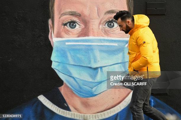 Pedestrian walks past graffiti by the artist @akse_p19, depicting an NHS nurse in scrubs and a face mask, but with an Angel's halo above her head, in...