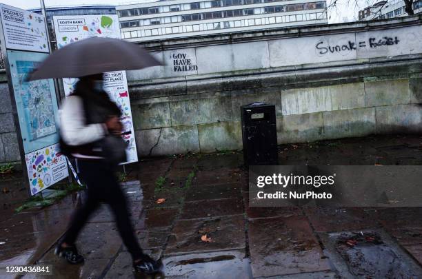 Woman wearing a face mask walks past anti-government graffiti on a wall outside St Thomas's Hospital in wet weather in London, England, on January 5,...