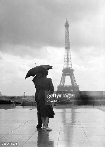 Couple embracing under an umbrella admire the Eiffel Tower on the Esplanade du Trocadéro under a cloudy sky during the particularly rainy summer of...