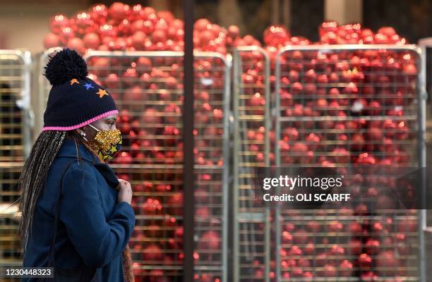 Pedestrian wearing a face covering walks past a Christmas baubles stored in crates inside a shop, temporarily closed down due to current coronavirus...