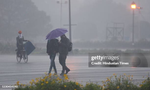 People use an umbrella to shelter themselves as they walk past Vijay Chowk amid rain and cold weather on January 6, 2021 in New Delhi, India....