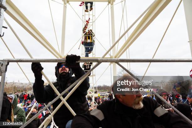 Protesters climb the scaffolding on the inauguration platform after breaking through barriers onto the grounds of the Capitol Building on January 6,...