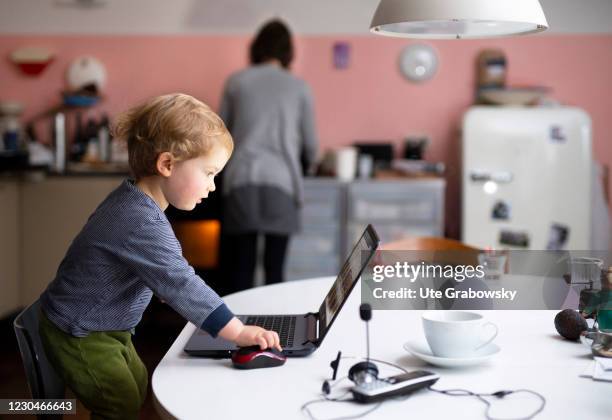 Bonn, Germany In this photo illustration a mother is doing homework while the child has climbed up a chair and is olaying with her laptop on January...