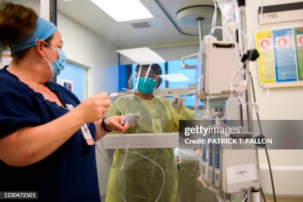 Nurse wearing personal protective equipment communicates through a glass door while attending to a patient in a Covid-19 intensive care unit at...