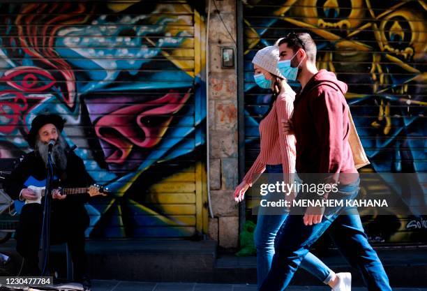 Couple, wearing protective masks due to the COVID-19 pandemic, walks past a guitarist at the Mahane Yehuda market in Jerusalem during a nationwide...