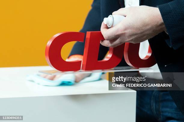 An employee cleans the podium while holding the CDU logo in a studio in Cologne, western Germany, on January 9, 2021 ahead of the virtual new year...