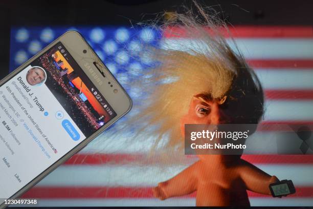 Donald Trump's Twitter account displayed on a mobile phone screen next to a vinyl doll which features the U.S. President Donald Trump, seen in front...