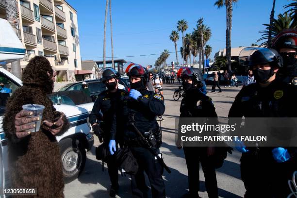 Person in costume speaks to San Diego Police Department officers as counter-protesters await to confront demonstrators during a "Patriot March"...