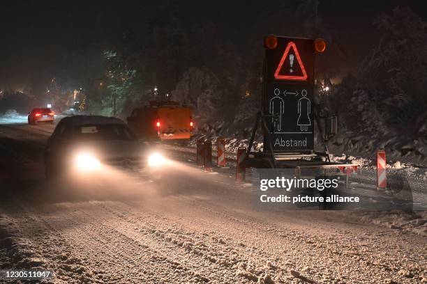 January 2021, Lower Saxony, Torfhaus: Vehicles drive past a traffic sign pointing out the need to keep their distance from the Torfhaus National Park...