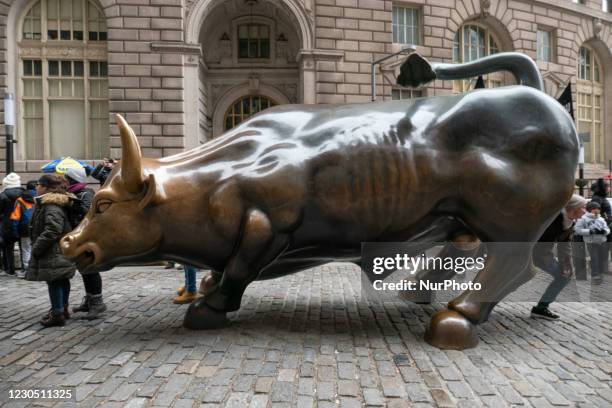 The Charging Bull bronze sculpture, also known as Wall Street Bull or Bowling Green Bull in New York City with tourists around taking photos of it as...