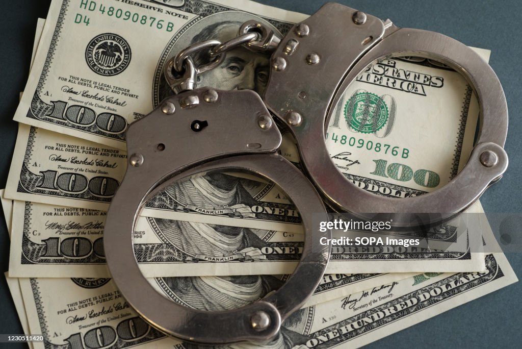 In this photo illustrations handcuffs and hundred us dollar...