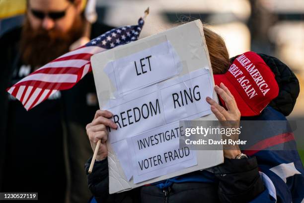 Supporter of President Donald Trump holds a MAGA hat and sign reading "Let freedom ring, investigate voter fraud" as conservative demonstrators...