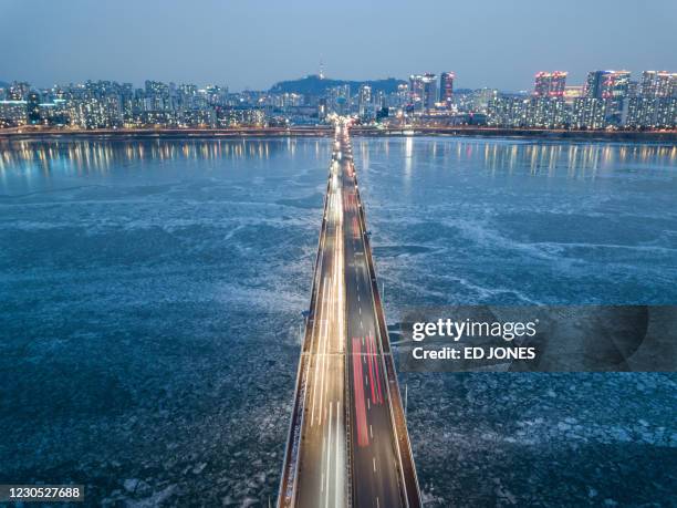 Photo taken on January 10, 2021 shows a general view of traffic passing over a bridge above the frozen Han river, before the Seoul city skyline.