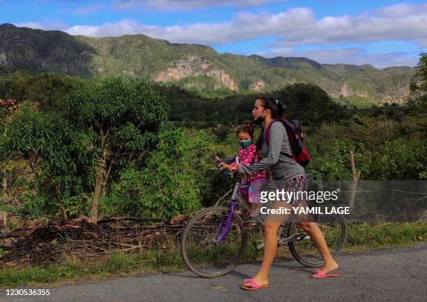 Cuban woman walks with her child in a bicycle along a road in Vinales, Pinar del Rio province, Cuba, on January 10, 2021.