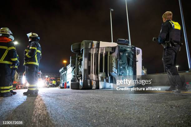 January 2021, Hamburg: Firefighters and a policeman stand next to the overturned articulated lorry on the 7 motorway. A lorry overturned in front of...