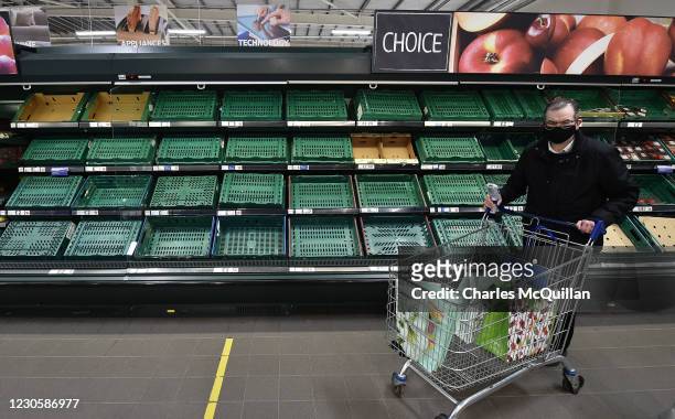 Supermarket shoppers walk past rows of empty shelves in Tescos on January 14, 2021 in Belfast, Northern Ireland. Supermarkets here are already seeing...